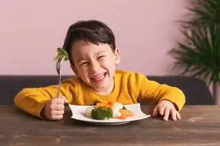 Ребенок улыбается во время еды тарелки с овощами
