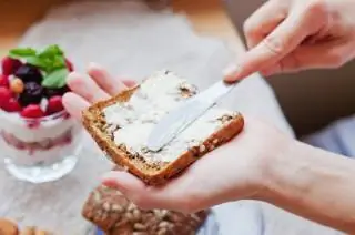 Женщина смазывает маслом цельнозерновой хлеб Женщина смазывает маслом цельнозерновой хлеб