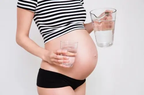 Крупным планом милый беременный живот со стаканом воды Крупным планом милый беременный живот со стаканом воды